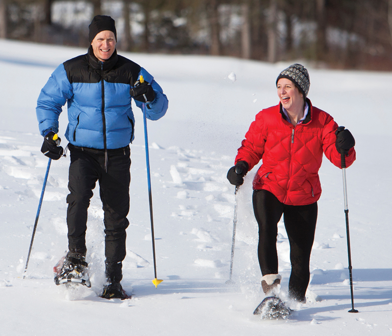 Man in blue jacket and woman in red jacket snowshoeing in winter